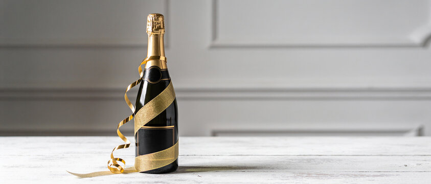 Black champagne bottle with gold ribbon and curling paper streamers standing on a white wooden table