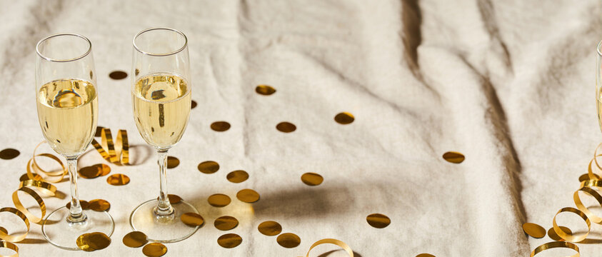 Two flutes of champagne and gold confetti on a textured beige cloth for a festive setting