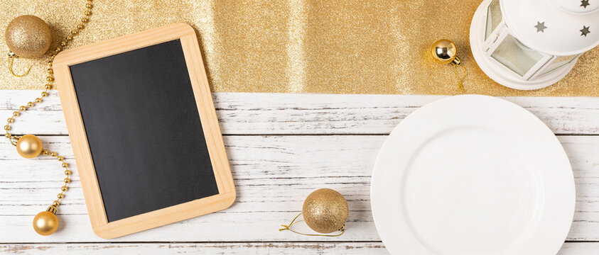 Festive flat lay with chalkboard, white plate, and gold ornaments on rustic wood background