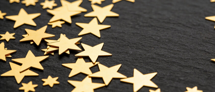 Gold star confetti scattered on a black textured surface with copy space at the bottom.
