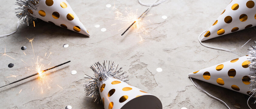 Gold polka dot party hats with tinsel and sparkling sparklers on a grey surface
