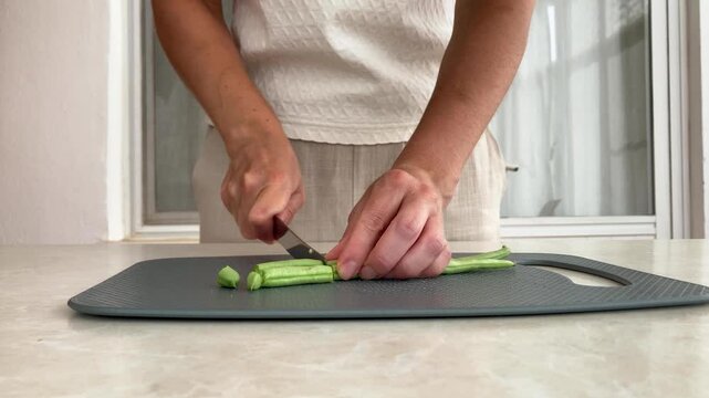 Women&rsquo;s hands are cutting green beans with a metal knife on a gray cutting board; the chef is preparing a dish from fresh seasonal vegetables, a harvest from the farm, home‑cooked food, a healthy diet