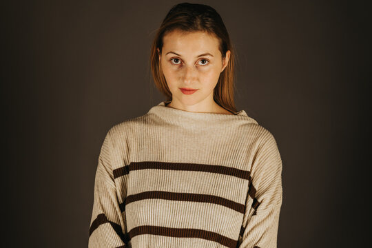 Young woman models a striped sweater in a studio portrait against a plain dark grey background for fashion and apparel use.