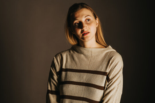 Woman looks away in a dark studio portrait wearing a striped knit sweater for fashion and apparel advertising with a thoughtful expression.