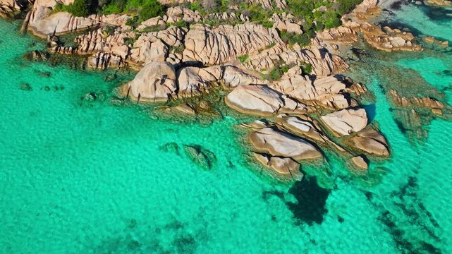 Top-down drone view of Spiaggia Testa del Polpo in Sardinia. Clear turquoise water, granite rocks and sandy seabed create a striking Mediterranean beach pattern.