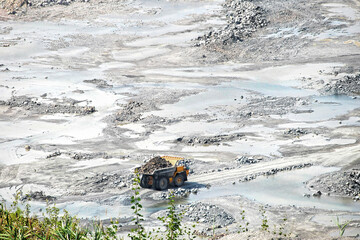 Yellow haul dump truck loaded with rock driving through quarry with water puddles and green grass © Volha Kliukina