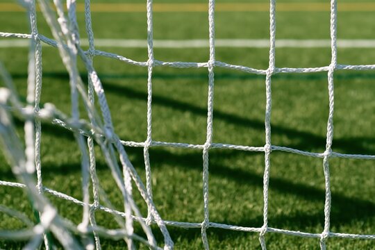 Close-up of knotted white football net with grass and shadows