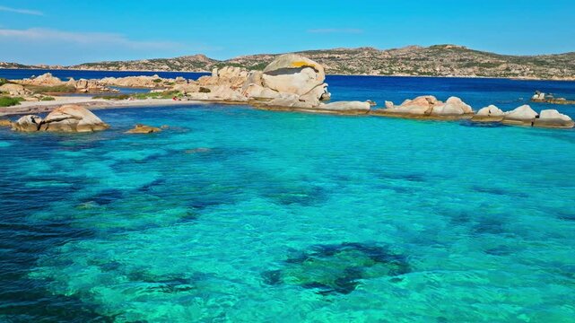 Aerial view of Spiaggia Testa del Polpo in La Maddalena, Sardinia. Tourists relax near granite rocks, crystal-clear turquoise water and shallow seabed, creating a beautiful Mediterranean beach scene.