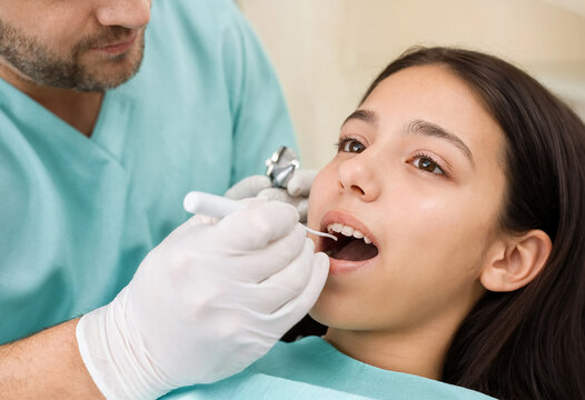 Dentist in protective gloves examines a young woman's teeth during an oral checkup at a dental clinic.