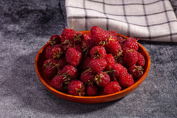 Fresh raspberries in wooden bowl on textured dark surface with checkered cloth background © Andrei Starostin