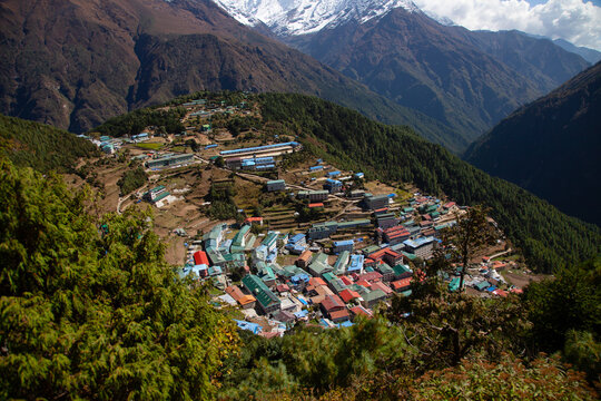 Mountains surround a small village with colorful buildings in a remote area, with snow-capped peaks in the background on a sunny day