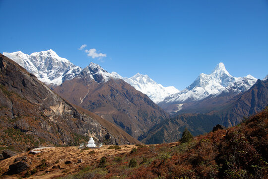 Snow-capped mountains rise above a white stupa in a valley during clear weather in the Himalayas