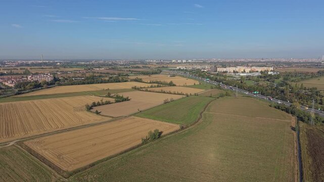 Rural Landscape and Cityscape Horizon: An aerial view showcases a patchwork of cultivated fields and green spaces transitioning towards a distant urban skyline under a clear blue sky.