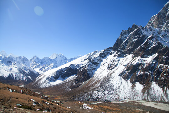 Snow-covered mountains and valleys in a high-altitude region during daytime with clear blue sky and bright sunlight