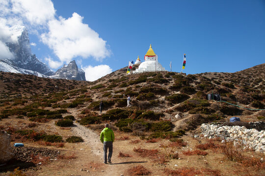 Man walks toward stupa on mountain path with snow-capped peaks and blue sky in Nepal on a clear day