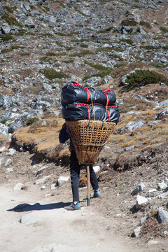 Worker carries heavy load on a path in the mountains during day