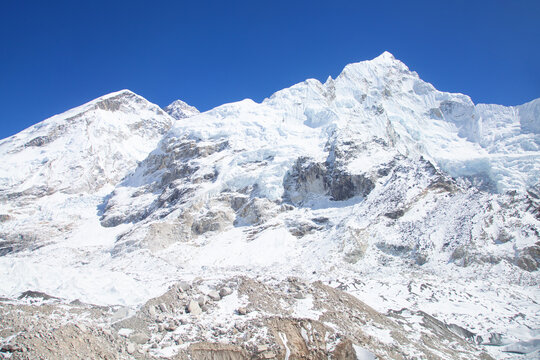 Snowy mountain range under clear blue sky with rocky ground below