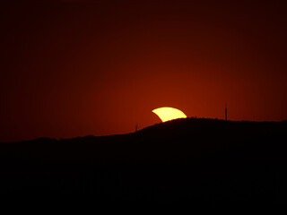 Partial solar eclipse on August 12, 2026, north of Dornheim in Thuringia, Germany. A slender solar crescent disappears behind a hill. A striking arc of light appears along the horizon. © Frank