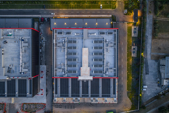 Aerial view of Aruba Hyper Cloud Datacenter IT4 featuring rows of cooling units and solar panels on the rooftop, with surrounding paved access roads and perimeter lighting Roma, Lazio, Italy.