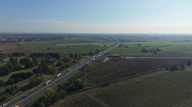 Aerial view of trucks and passenger vehicles traveling along a busy motorway in northern Italy. The scene illustrates road infrastructure
