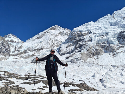 Hiker stands on rocky ground with snow-covered mountains in the background on a clear day in the Himalayas