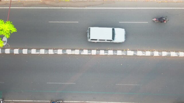 Malang, East Java, Indonesia - 09 October 2026: Aerial view of traffic on a road with motorcycles and a car moving along the asphalt surface.