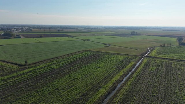 Vast Agricultural Landscape: An expansive aerial view showcases a patchwork of green fields, farmland, and a small irrigation channel under a clear blue sky.
