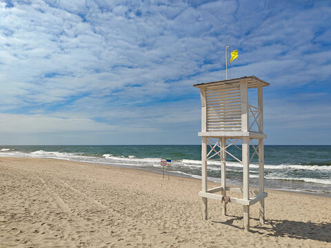 Lifeguard tower stands on sandy beach with waves and clouds in the background