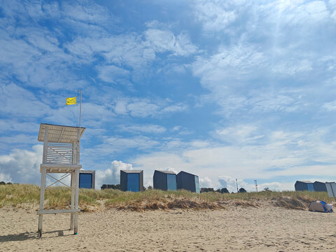 Lifeguard tower overlooks beach and beach huts on a sunny day