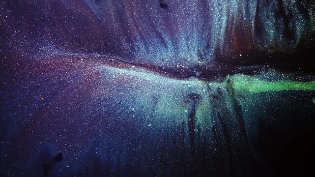 Sparkling green ink forms a sweeping stream through violet liquid as pigment flecks drift outward in a cosmic-style pattern.