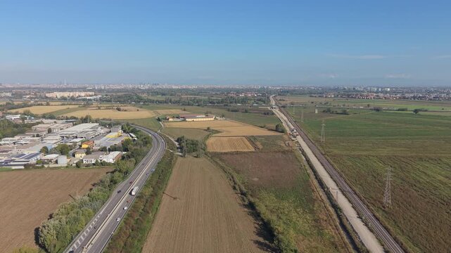 Aerial view of an industrial area bordered by a highway and railway infrastructure, with an existing rail line and a new railway under construction. 