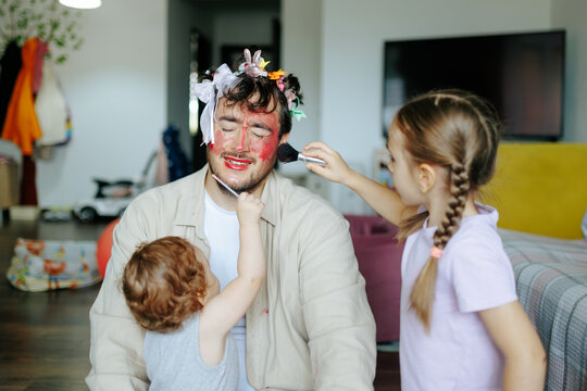 Single father smiling while little girl applies bright lipstick. Playful parenting at home