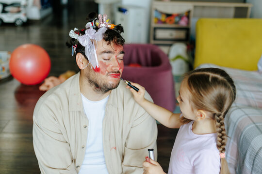 Young sisters playing pretend beauty salon decorating father face. Creative child development