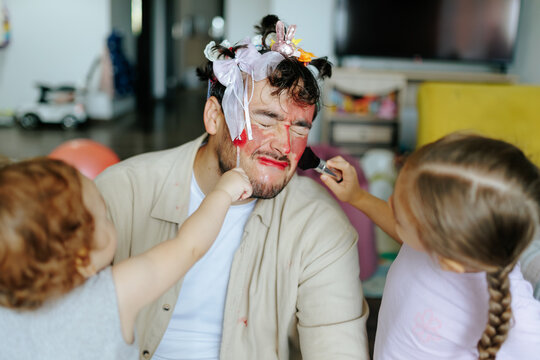 Girl dad wearing colorful hair clips placed by young daughter. Playful makeover family humor