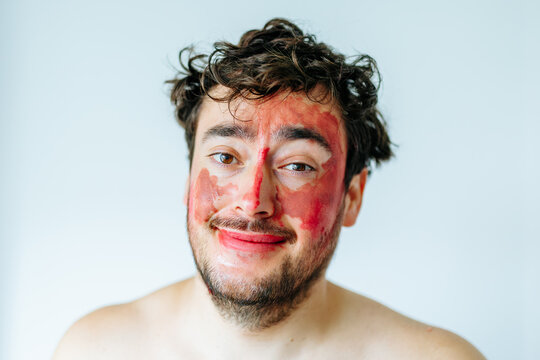 Smiling man with colorful face paint looking at camera. Playful studio portrait and happy humor