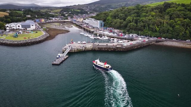 Aerial view of a passenger ferry boat arriving at Bantry Harbour pier in County Cork Ireland. Aerial footage of Bantry coastal town landscape with marina with moored yachts, waterfront buildings.