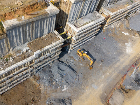 Aerial view of a construction site with a yellow excavator working near a deep excavation pit supported by concrete retaining walls and metal struts in Istanbul, Istanbul, Turkiye.