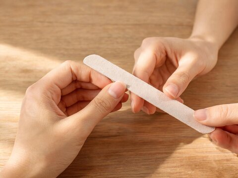 Woman filing fingernails with emery board at table