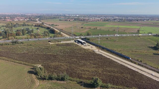 Aerial view of a new railway construction site alongside a major highway in northern Italy, including a railway tunnel under construction.