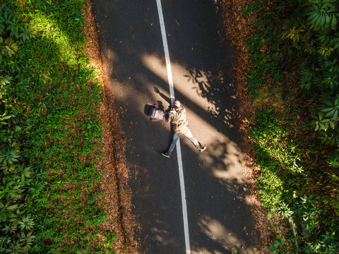 Aerial view of a person lying on a paved road with a backpack in a lush forest in Baturaden, Central Java, Indonesia.
