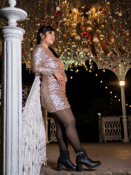 Woman in Elegant Dress Posing at a Festive Christmas Gazebo at Night