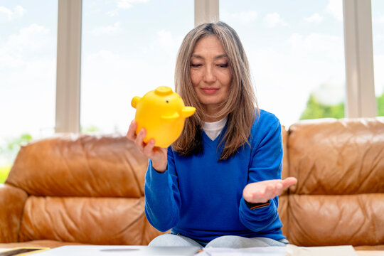 Woman holding a yellow piggy bank while sitting on a couch indoors
