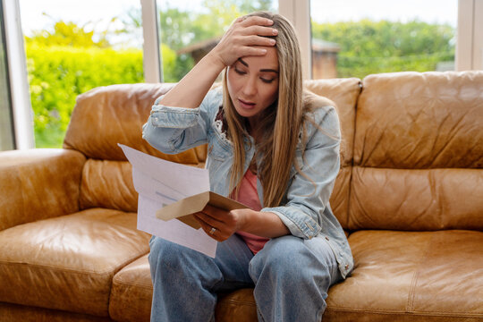 Woman sitting on couch looks worried while reading a letter in brown envelop in a bright living room