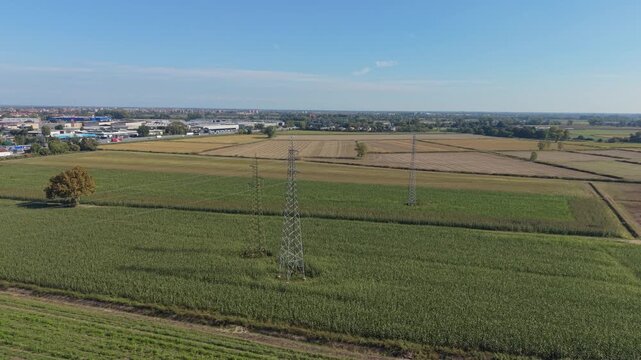 Aerial view of overhead power transmission lines extending across cultivated farmland in Lombardy, Italy.