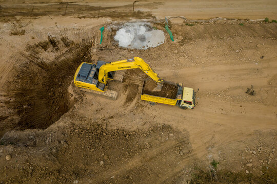 Aerial view of a yellow excavator loading soil into a dump truck at a construction site in Salatiga, Central Java, Indonesia.