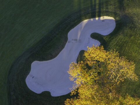 Aerial view of a sand trap on a golf course in autumn with vibrant yellow foliage on a nearby tree and green grass in Glenview, Illinois, United States.