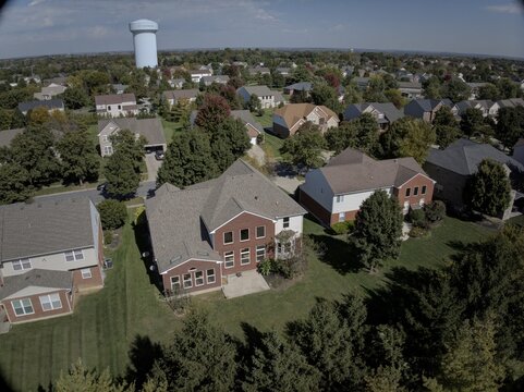 Aerial view of a residential neighborhood featuring suburban houses, manicured lawns, mature trees, and a distant water tower under a clear blue sky in Mason, Ohio, United States.