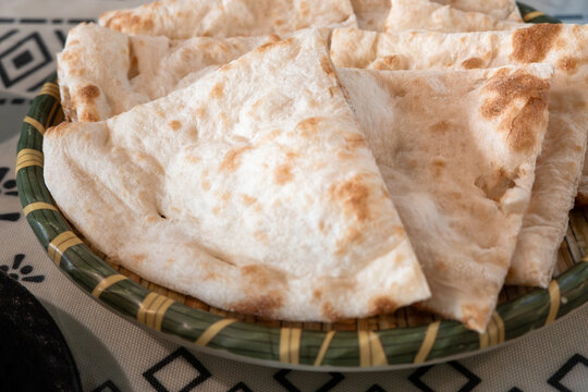 Fresh baked Indian naan flatbread slices served on a woven plate.