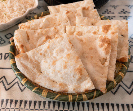 Fresh baked Indian naan flatbread slices served on a woven plate.