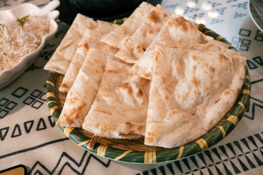 Fresh baked Indian naan flatbread slices served on a woven plate.